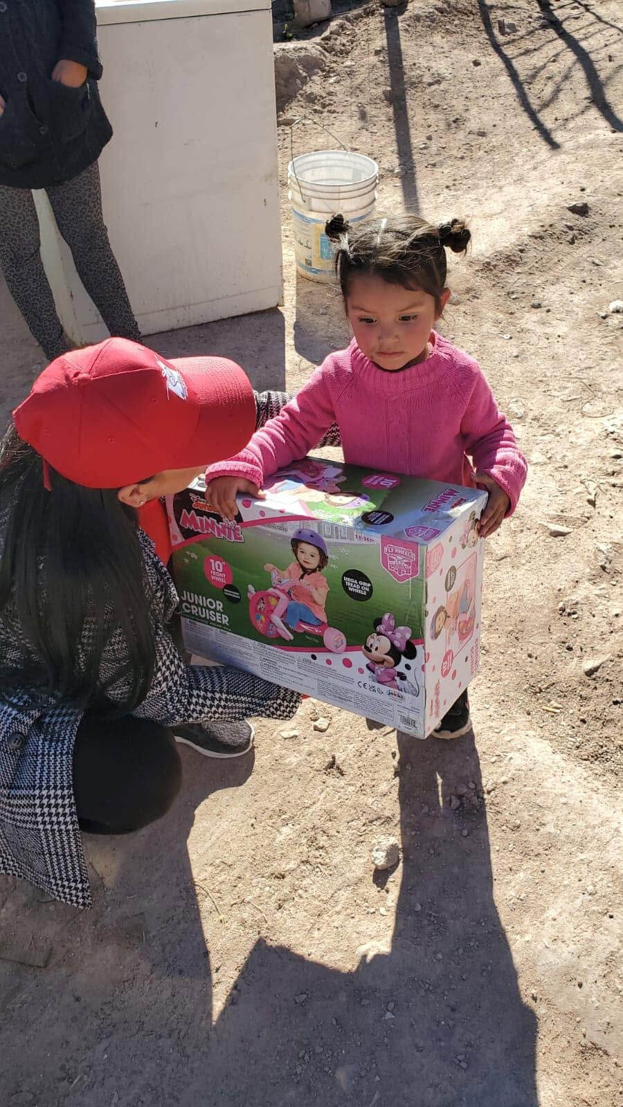 Una voluntaria entrega una caja de juguetes envuelta a una niña